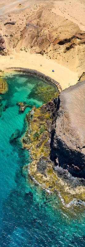 Flygvy över Papagayo-stranden på Lanzarote, med gyllene sand, vulkaniska klippor och turkostfärgat hav.