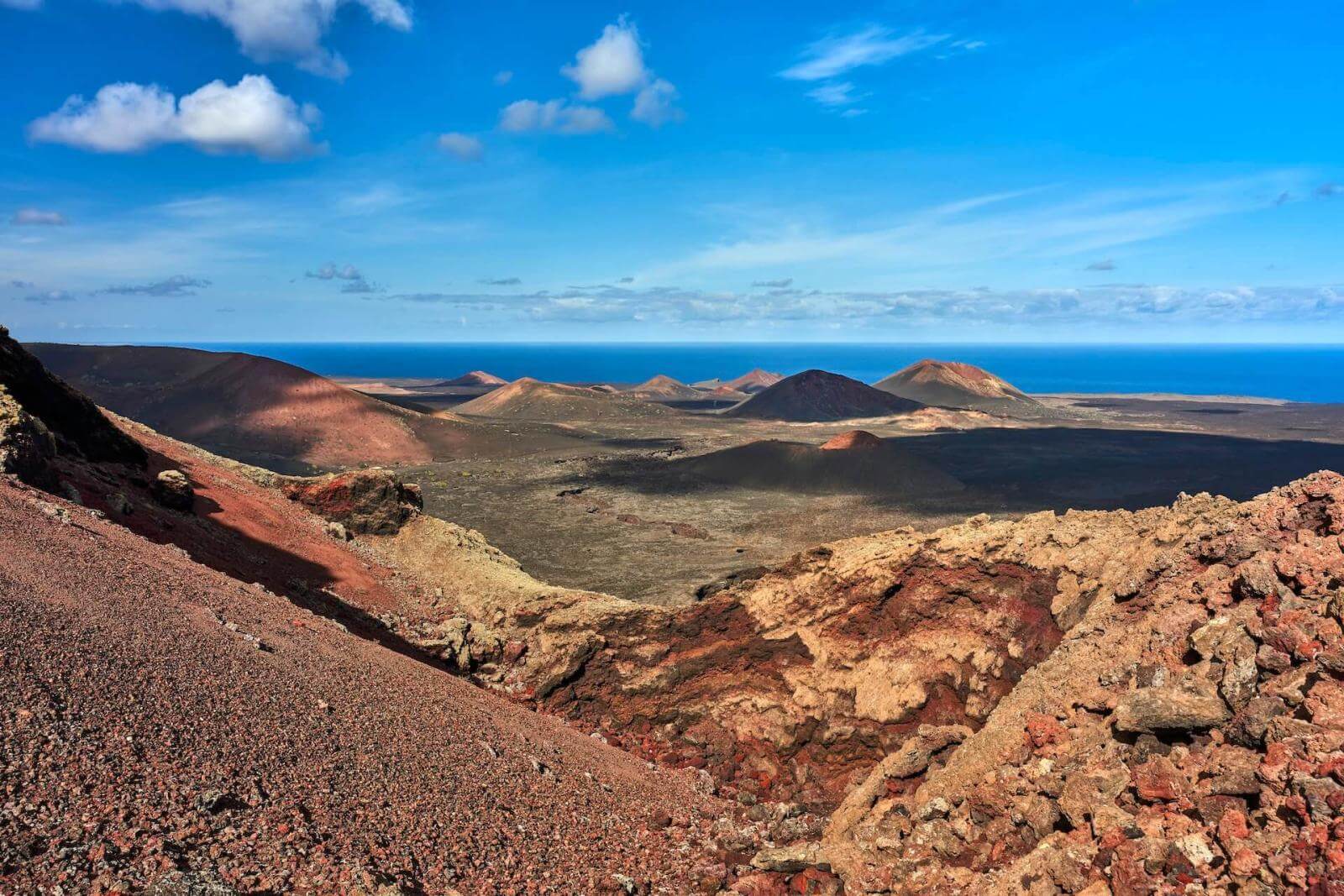 Vulkaniskt landskap med stora lavatäcken i nationalparken Timanfaya, Lanzarote, i bakgrunden ses berg och hav.